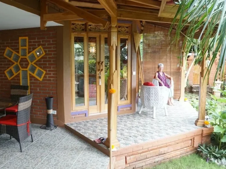 Gemütliche Terrasse mit einem Mann an einem Tisch, umgeben von Pflanzen und Holzstruktur.