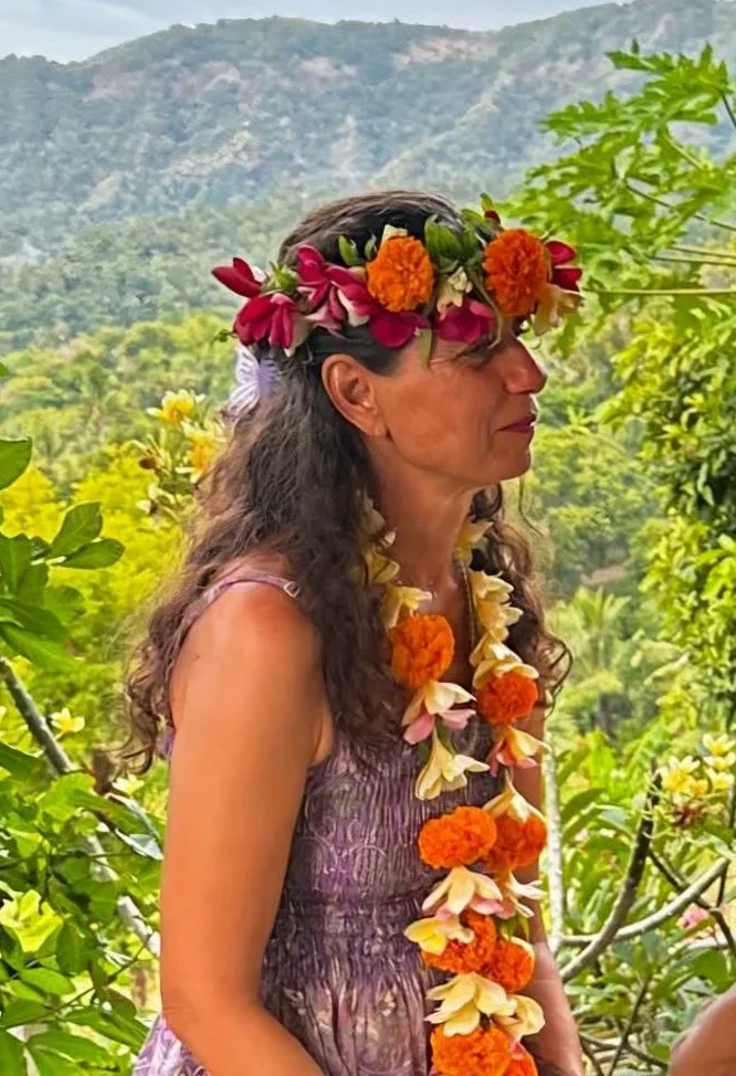 Frau mit Blumenkranz und Leih in einer tropischen Landschaft.
