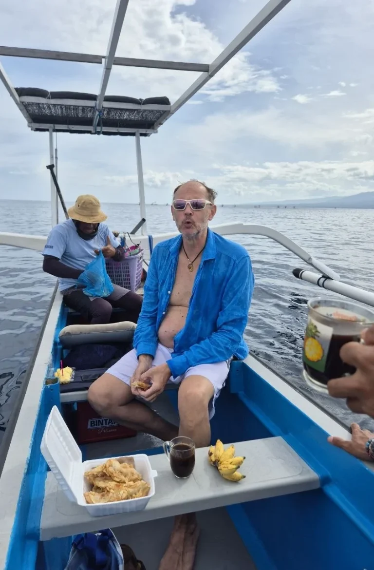 Mann sitzt auf einem Boot, genießt Snacks und ein Getränk, umgeben von Wasser und Himmel.