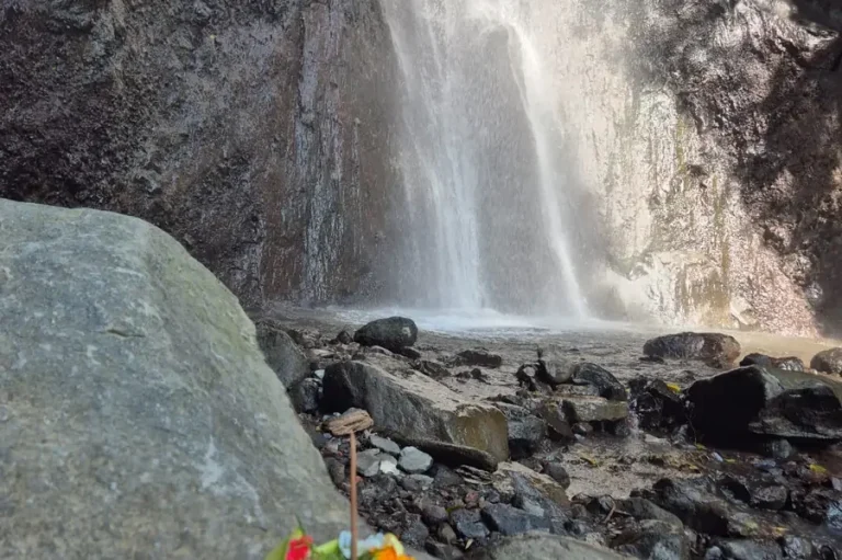 Wasserfall neben Steinen, mit bunten Blumen im Vordergrund.