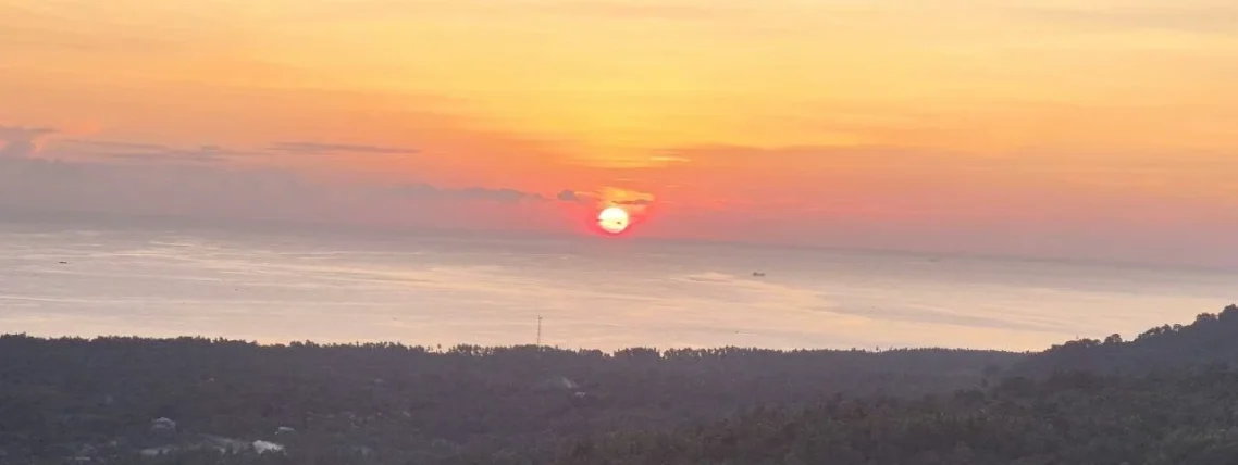 Sonnenuntergang über dem Meer, rosa-orangefarbener Himmel und silhuettierte Küstenlinie.