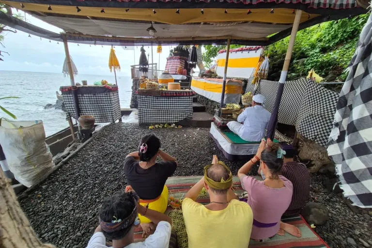 Personen sitzen auf dem Boden und betrachten eine Zeremonie am Strand.
