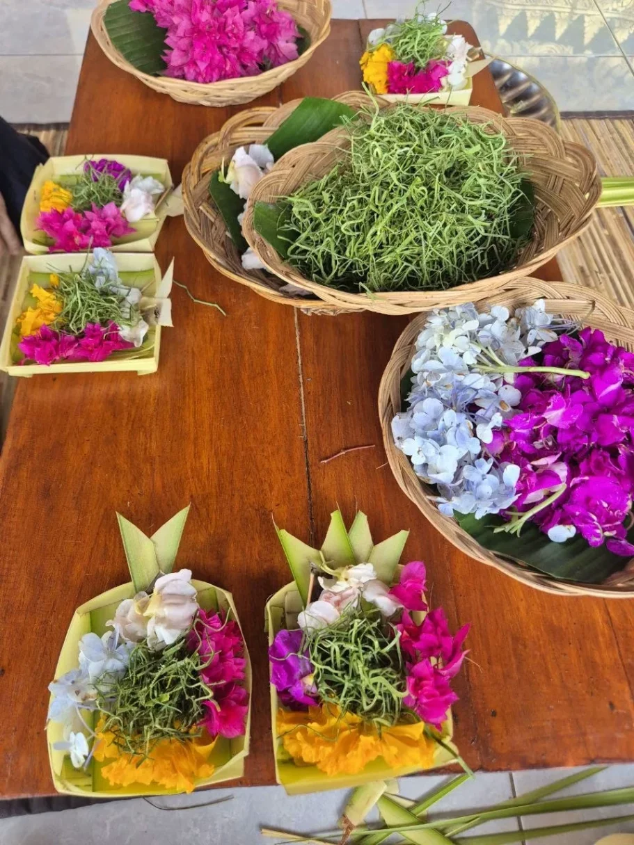 Bunte Opfergaben aus Pflanzen und Blumen, arrangiert auf einem Holztisch.