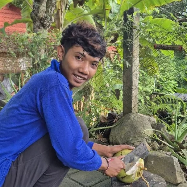 Junger Mann in blauer Jacke schneidet Obst im Freien, umgeben von Pflanzen.