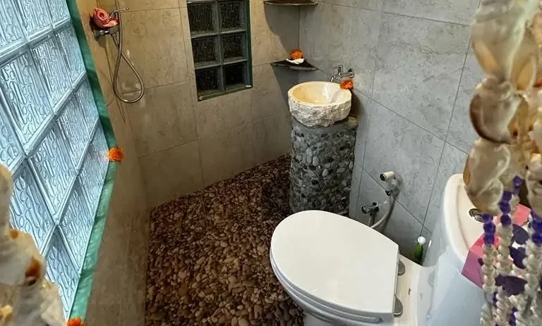 Toilet in einem Badezimmer mit steinartigem Bodenbelag und dekorativen Elementen.