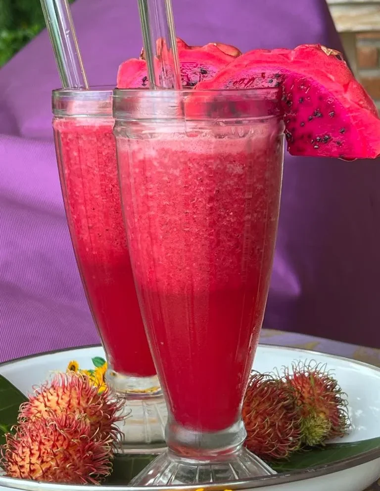 Zwei pinkfarbene Getränke mit einer Drachenfrucht und Rambutan auf einem Teller.
