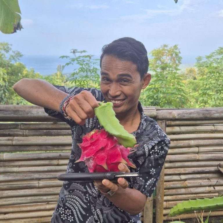 Ein Mann hält eine Teller mit einer Drachenfrucht und schneidet sie mit einem Blatt.