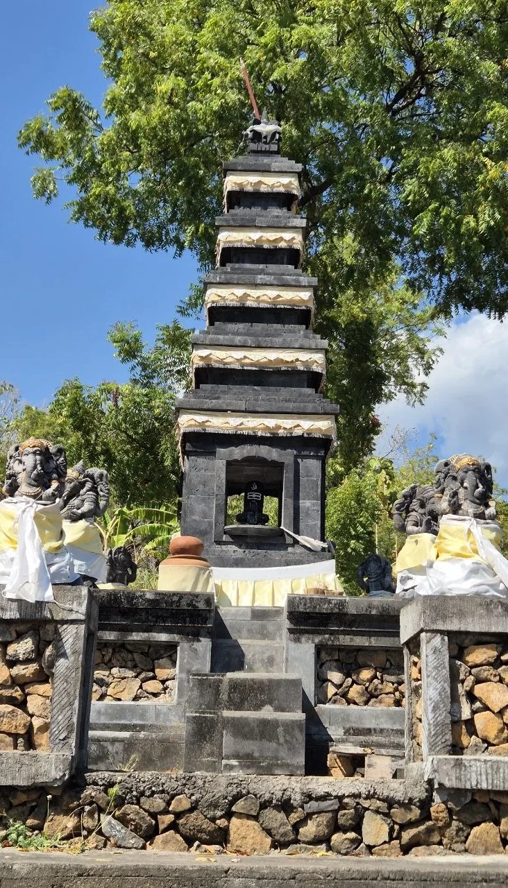 Steinerner Tempel mit mehreren Ebenen, umgeben von Bäumen und Skulpturen.