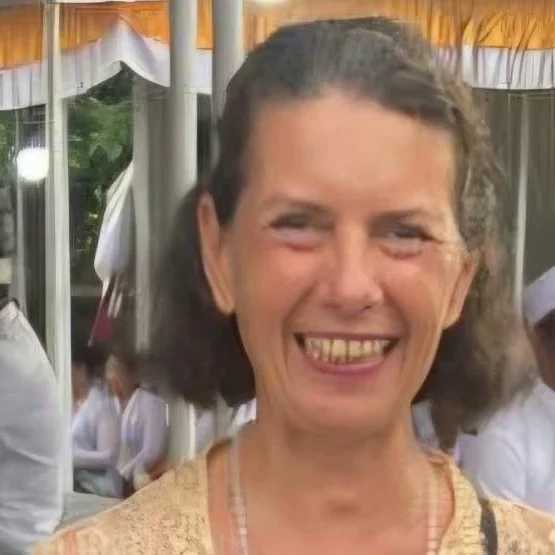 Lächelnde Frau mit dunklem Haar und heller Bluse, vor festlicher Kulisse.